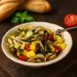 Een kleurrijke salade met stukjes alfícoz, mango, rode ui, tomaat en verse koriander, geserveerd in een witte schaal op een bamboemat.