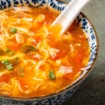 Een kom met authentieke Chinese tomatensoep, gegarneerd met lente-uitjes en geserveerd met een witte porseleinen lepel.