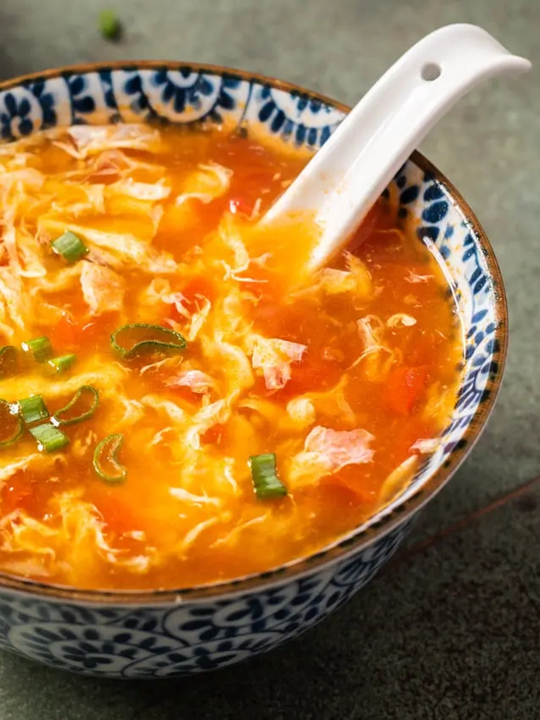 Een kom met authentieke Chinese tomatensoep, gegarneerd met lente-uitjes en geserveerd met een witte porseleinen lepel.