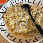 Een grote schaal met romige pasta Gorgonzola, versierd met champignons, gehakte peterselie en geraspte Parmezaanse kaas, geserveerd in een wit bord met het woord 'Pasta' erop.