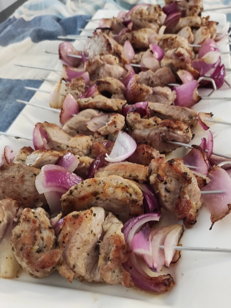 Souvlaki spiesen met gemarineerd varkensvlees en rode ui, gegrild tot perfectie en gepresenteerd op een wit bord.