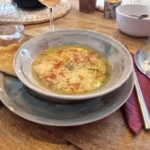 Stracciatella alla Romana, een lichte Italiaanse soep met ei, Parmezaanse kaas en kruiden, geserveerd in een rustieke kom, vergezeld van brood en een glas rosé op een houten tafel.
