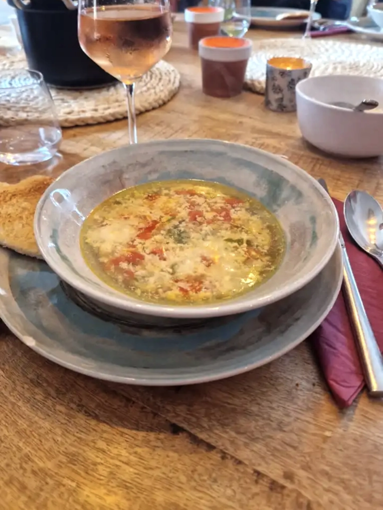 Stracciatella alla Romana, een lichte Italiaanse soep met ei, Parmezaanse kaas en kruiden, geserveerd in een rustieke kom, vergezeld van brood en een glas rosé op een houten tafel.