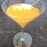 Een martiniglas gevuld met huisgemaakte advocaat, gegarneerd met een toef slagroom en een lepel, op een donkere achtergrond.
