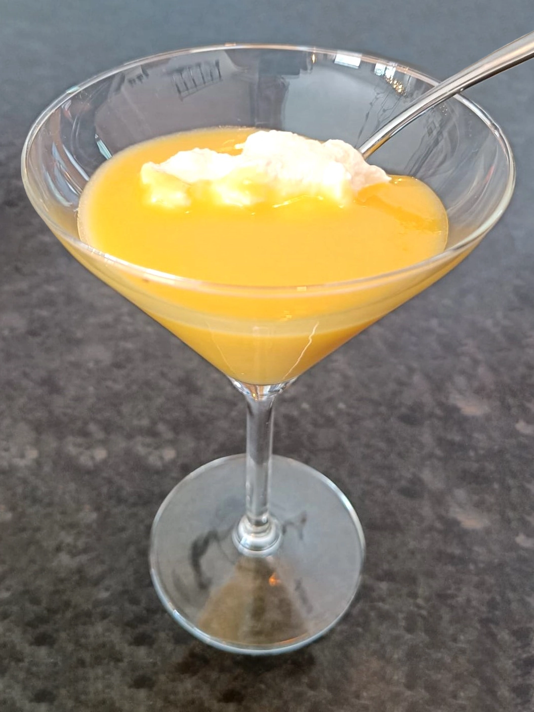 Een martiniglas gevuld met huisgemaakte advocaat, gegarneerd met een toef slagroom en een lepel, op een donkere achtergrond.