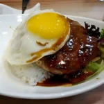 Een bord met Loco Moco, een Hawaiiaans gerecht bestaande uit witte rijst, een hamburgerpatty met bruine jus, en een gebakken ei.