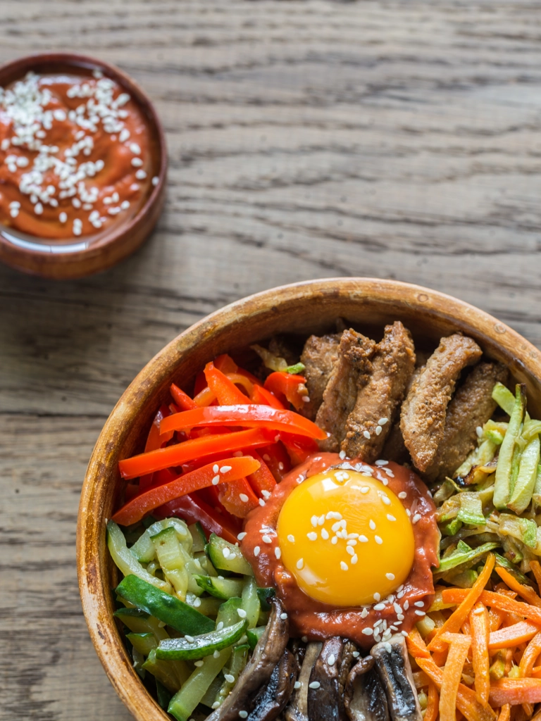 Koreaanse bibimbap in een kom op een houten tafel met een klein schaaltje met saus