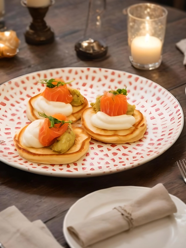 Blini's met zalm op een licht gekleurd bord op een mooi gedekte tafel