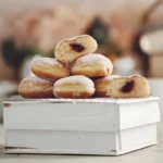 Krofne, heerlijke Kroatische donuts op een wit houten kistje, de lekkere vulling van jam is goed te zien in de doorgesneden krofne.