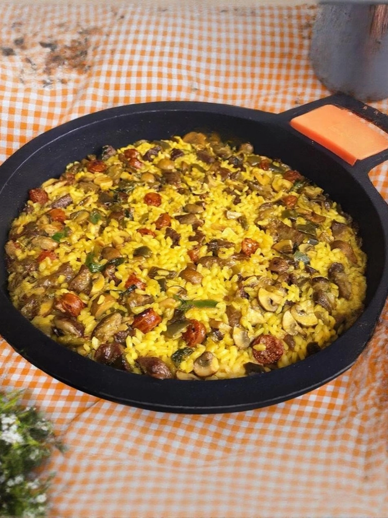 Een prachtig gekleurde paella de secreto met groenten in een grote paella pan op een oranje geruit kleed.
