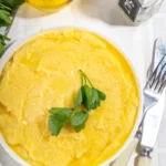 Mooi geel gekleurde polenta in een wit schaaltje met een takje peterselie erop.